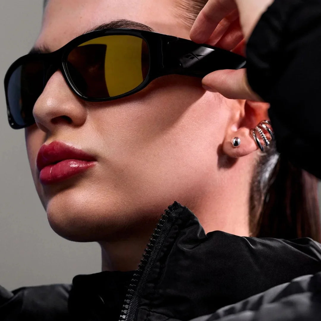 Primer plano de mujer ajustando gafas deportivas con lentes amarillas; mostrando el detalle de la patilla y los altavoces.